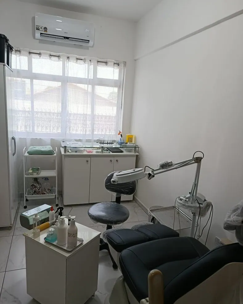 Sala do consultório de podologia, clara, com cadeira podológica reclinável, foco de luz e bancada de apoio